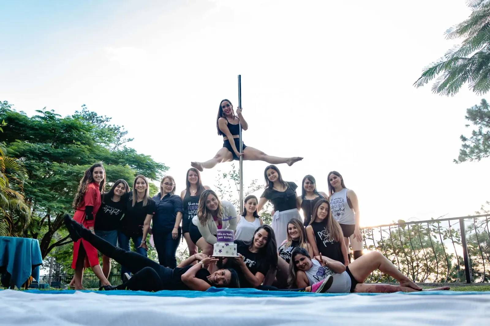 Quince mujeres alrededor de una barra en un jardín con montañas al fondo