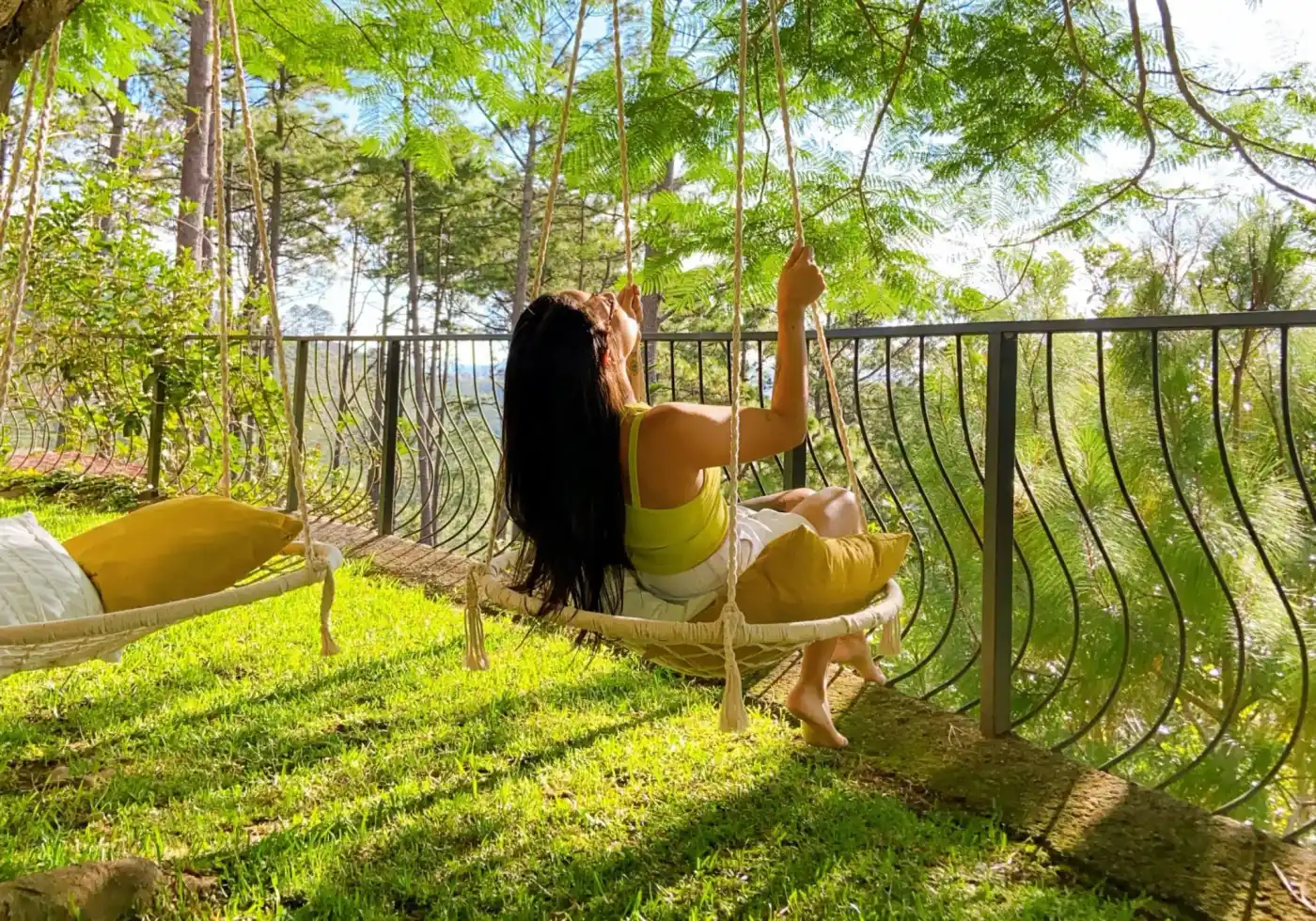Mujer de espaldas descansando en una hamaca en una terraza con árboles